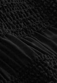Tissu noir avec un design texturé et froncé, présentant des bords ondulés. Des sections lisses alternent avec des sections étroitement froncées, créant un contraste.