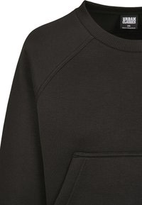Felpa nera con colletto a girocollo, maniche raglan e tasca frontale. Realizzata in un tessuto liscio ed elastico con scollatura a costine.