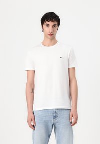 T-shirt en coton blanc à manches courtes et encolure ronde. Présente un petit logo sur la poitrine et est assortie à un jean bleu clair.
