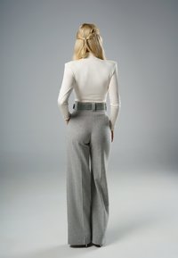 Biała dopasowana bluzka z długim rękawem zestawiona z wysokimi spodniami w kolorze szarym o szerokich nogawkach, charakteryzującymi się fakturowanym materiałem i kontrastującym paskiem.