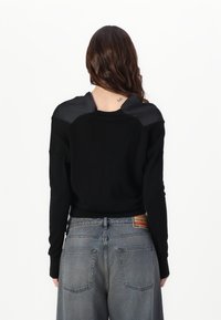 Czarny sweter z satynowym detalem na ramieniu, zestawiony z wysokim stanem spodni jeansowych w kolorze wyblakłej szarości, posiadających dwie tylne kieszenie i kontrastowe przeszycia.