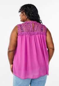 Fuchsiasfärgad ärmlös blus med en texturerad broderad baksida och en nyckelhålsöppning, tillverkad av lätt, flödande tyg.