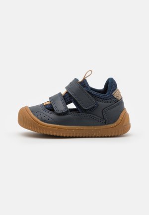 Navy blue lasten kengät, joissa on kumi- ja verkko-paneelit sekä kaksi säädettävää tarranauhaa. Ominaisuutena teksturoitu kantapään koriste.