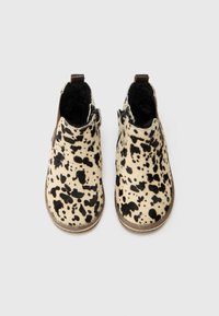 Botines de piel de vaca con base crema y patrones de manchas negras, superficie texturizada y acentos marrones en el talón y la cremallera.