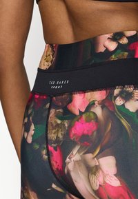Juodos aukšto liemens leggingai su daugiaspalviu gėlių raštu. Yra juodas elastinis juosmuo su baltu „TED BAKER SPORT“ prekės ženklu.