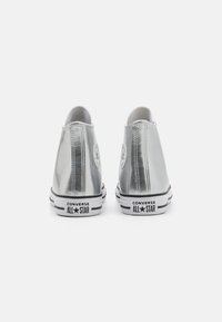 Hõbedased hi-top sneakersid läikiva viimistlusega, valge voodriga, mustade talladega ning musta ja valge Converse All Star logo'ga kandadel.