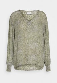Blouse verte à manches longues avec un décolleté en V, ornée d'un motif floral blanc et de poignets élastiques. Fabriquée en tissu léger et texturé.