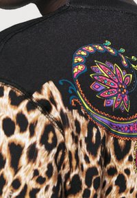 T-shirt med leopardmönster och svarta samt färgglada prydnader. Har stretchiga partier av mjukt tyg och synliga sömmar.