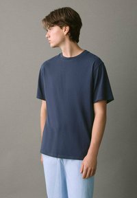 Tummansininen pyöreäkaula-aukko t-paita puuvillakankaasta, lyhyet hihat, rento istuvuus. Yhdistetty vaaleaviiruisiin housuihin. Yksinkertainen ja monikäyttöinen muotoilu.