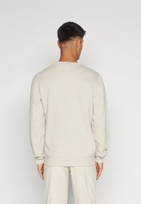 Lys beige sweatshirt, rund hals, ribbede manchetter og kant, blød tekstur, afslappet pasform. Båret med matchende bukser, set fra ryggen.