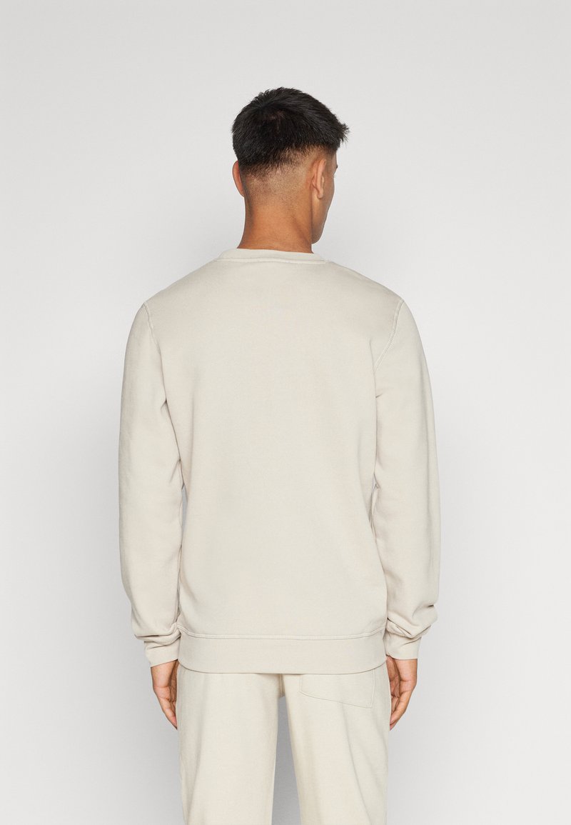 Sweatshirt beige clair, col rond, poignets et ourlet côtelés, texture douce, coupe décontractée. Porté avec un pantalon assorti, vu de dos.