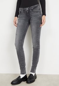 Jeans ajustados grises de mezclilla con un lavado desgastado y detalles sutiles de desgaste, combinados con mocasines negros y calcetines blancos.