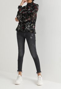 Black sheer blouse with floral print and ruffled cuffs, paired with distressed dark jeans and white sneakers. Casual outfit combination.