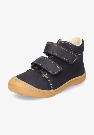 Black leather boot with two Velcro straps, beige sole, rounded toe, and white stitching detail. Soft interior lining for comfort.