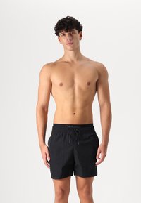 Čierne plavky z ľahkého materiálu s elastickým pásom a šnúrkou, na ktorej je umiestnené malé logo Calvin Klein.