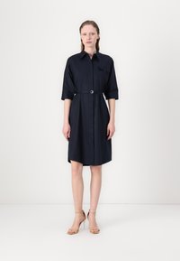 Navy blue shirt dress with a collar, three-quarter sleeves, and a belted waist. Features a button-up front and single chest pocket.