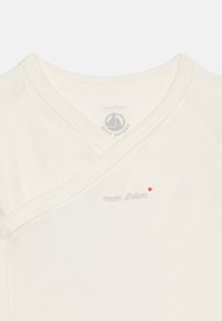 Λευκό κορμάκι με κουμπιά κούμπωματος, γκρι κείμενο "mon trésor" και μικρή κόκκινη καρδιά κοντά στη λαιμόκοψη, μέγεθος 12 μηνών/74 εκ.