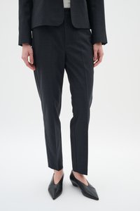Tamno sivi krojeni hlače izrađene od teksturiranog materijala, sa slim fit krojem i precrtanim linijama, uparene s crnim cipelama na visoku pete s oštrim vrhom.
