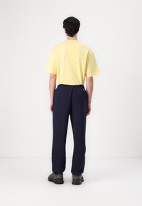 Yellow cotton t-shirt with short sleeves paired with navy blue elastic-waist pants. Black sneakers are worn, showing a simple, casual outfit.