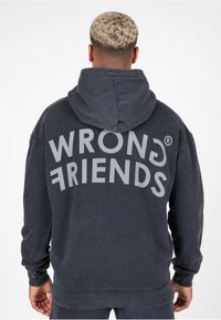 Sudadera con capucha de color gris oscuro que presenta un gran texto "WRONG FRIENDS" en la parte posterior en color gris claro. Tejido suave con un ajuste relajado y bolsillo tipo canguro.