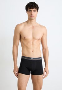 Boxers noirs en tissu doux avec un design ajusté. La ceinture contrastée présente le logo "BOSS" en gris. Texture lisse, longueur de jambe courte.