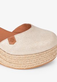 Chaussure à plateforme avec un dessus en tissu beige pailleté, bout arrondi, semelle en jute tressé et une étiquette en cuir sur le côté.