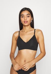 Bralette sans fil noir avec un design en V, bretelles fines ajustables et texture lisse. Présente un logo Calvin Klein sur la bande.