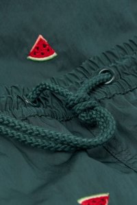 Tejido de color verde oliva con detalle de cordón, que presenta un bordado de una rebanada de sandía. Textura suave con cintura fruncida para ajustar el calce.