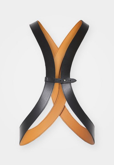 Leather harness in black and tan, featuring cross-pattern design, smooth texture, and a single adjustable strap with a metal snap closure.