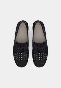 Μαύρα παπούτσια από σουέντ με στρογγυλή μύτη, υφή με μεταλλικά τρουκς στο μπροστινό μέρος και λεπτές, ραμμένες λεπτομέρειες στις πλευρές.