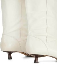 White leather ankle boots with a pointed toe, low kitten heels, and smooth texture. Features stitched detailing at the seams.