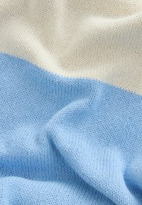 Pletená deka s horizontálnymi pruhmi v svetlo modrej a krémovej farbe. Mäkkučký povrch, rovnomerne tkaný vzor s hladkým povrchom.