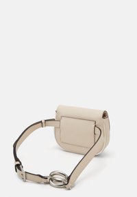 Beżowa skórzana torba o zakrzywionym kształcie. Posiada przednią kieszeń, regulowany pasek oraz srebrne akcenty metalowe. Gładka faktura.