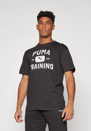 Zwarte katoenen T-shirt met "PUMA TRAINING" grafisch in het wit, korte mouwen, ronde hals, losse pasvorm, gedragen met bijpassende donkere broek.