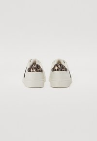 Hvite sneakers med et teksturert dyreprint-detall på hælen. Rund tåform, flate lisser og en teksturert gummisåle.