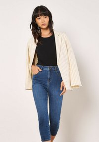 Blazer de talla grande a rayas crema, top negro de canalé, y jeans oscuros cortos. El blazer cuenta con mangas amplias y un cierre de botón único.