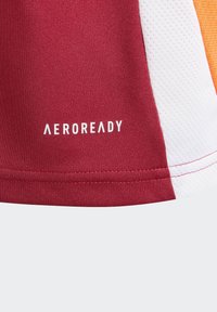 Tissu de sport rouge avec des panneaux blancs et orange, présentant une finition texturée. Logo "AEROREADY" imprimé en blanc.