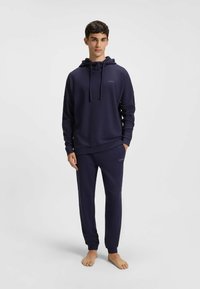 Granatowy zestaw bluzy z kapturem i spodni z fakturowanej tkaniny, z kapturem na sznurki oraz akcentami z logo na klatce piersiowej i udzie.