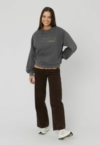 Sweat-shirt gris avec le texte "OUTSIDE", pantalon en velours côtelé marron et baskets blanches, debout devant un fond uni. Coupe décontractée et style relax.
