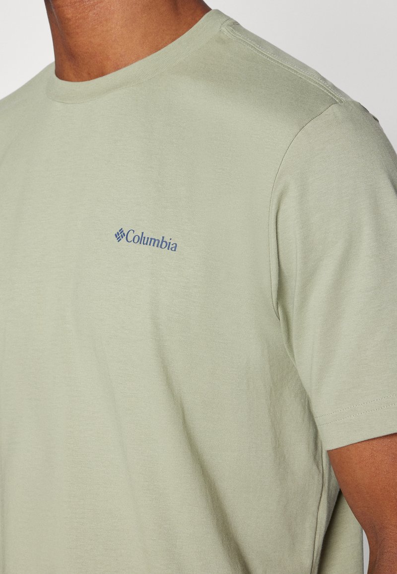 Jasnozielona koszulka z krótkim rękawem, uszyta z miękkiej tkaniny, z małym niebieskim logo Columbii na lewej piersi.