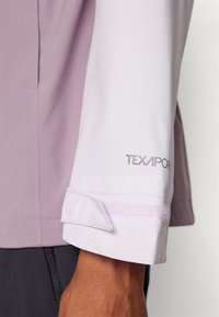 La manche de la veste TEXAPORE violet clair présente un pli en tissu texturé contrastant, avec une fermeture velcro au poignet.