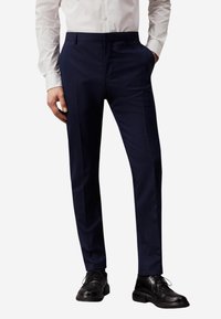 Pantaloni da uomo navy a vestibilità slim, realizzati in tessuto liscio. Presentano un frontale piatto, tasche laterali e una piega lungo le gambe, abbinati a scarpe nere.