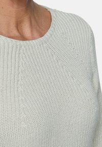 Lichtgrijze gebreide trui met een geribbelde textuur, voorzien van een ronde halslijn en subtiele naaddetails op de schouder.
