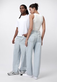 Baggy light blue denim jeans, a white tank top, and a plain white t-shirt. Close-fitting with slight stretch, showing back pocket details.