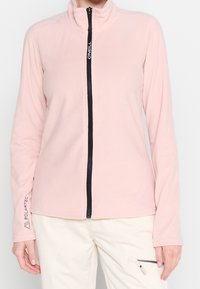 Rosa Fleecejacke mit hohem Kragen und vorne liegendem Reißverschluss. Verfügt über einen schwarzen Reißverschluss und Polartec-Branding auf dem Ärmel. Glatte Textur.