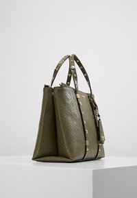 Olivengrønne håndtaske med præget mønster, struktureret overflade, dobbelt håndtag, spidse stropper og et lille dekorativt mærke.