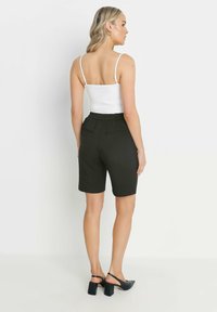 Svart, knälånga shorts med elastisk midja och två bakfickor, i kombination med en vit, figurnära linne och svarta klackskor med blockklack.