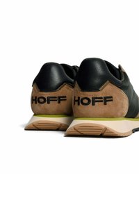 Zapatillas de cuero negro y ante beige con detalles en verde, que presentan una suela texturizada y la palabra "HOFF" en el talón.