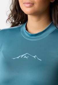 Turquoise athletic shirt with a smooth texture, featuring a white mountain graphic on the chest and a fitted, crew-neck design.