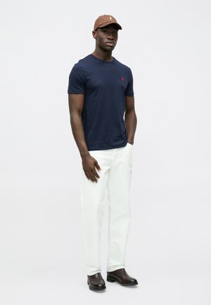 Μπλε μπλουζάκι με λογότυπο, άσπρο παντελόνι και καφέ μπέιζμπολ καπέλο. Ανθεκτικά καφέ μποτάκια. Ομαλό ύφασμα, άνετη εφαρμογή, απλός σχεδιασμός.